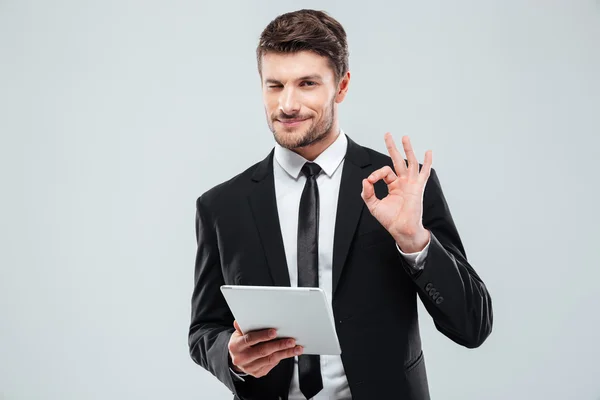 Felice giovane uomo d'affari con tablet ammiccante e mostrando segno ok — Foto Stock