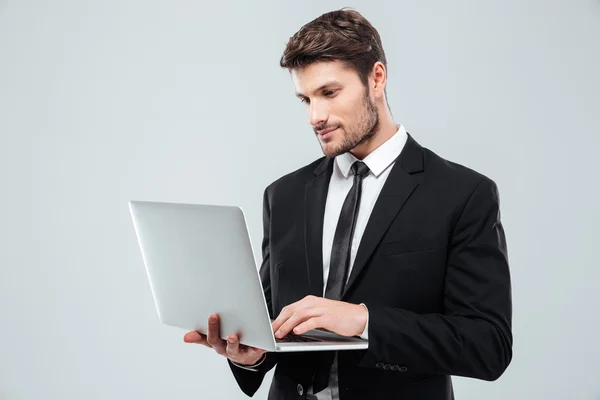 Knappe jonge zakenman permanent en het gebruik van laptop — Stockfoto