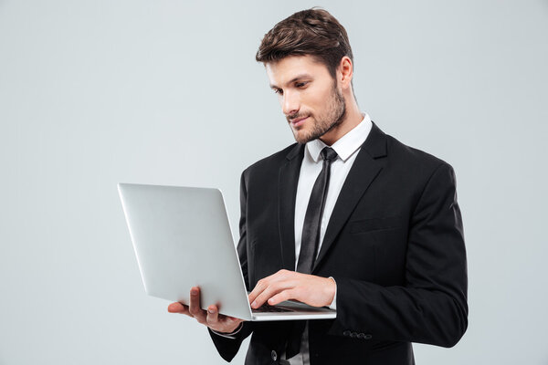 Handsome young businessman standing and using laptop