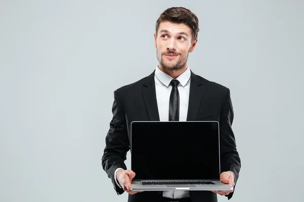 Pensive young businessman holding blank screen laptop and thinking — Stock Photo, Image