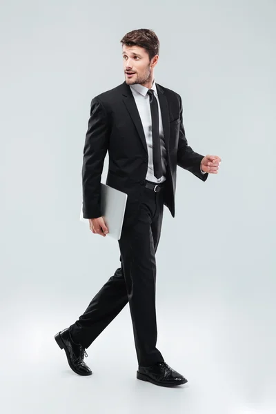 Повна довжина привабливого молодого бізнесмена, який ходить і тримає ноутбук — стокове фото