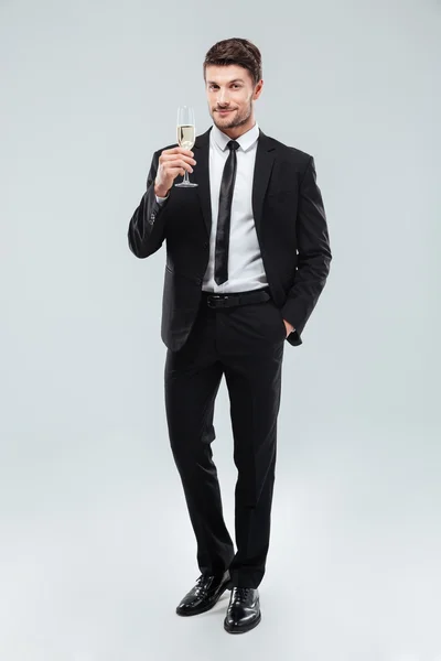 Lächelnder schöner junger Geschäftsmann steht und hält ein Glas Champagner in der Hand — Stockfoto