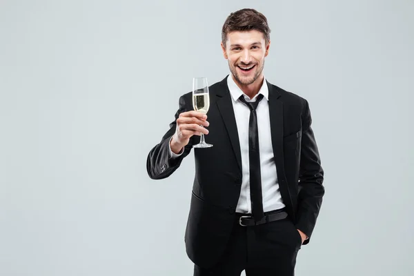 Улыбающийся молодой бизнесмен с бокалом шампанского стоя и празднуя — стоковое фото