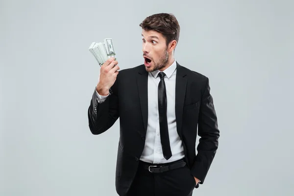 Потрясенный молодой бизнесмен, стоящий и держащий деньги — стоковое фото