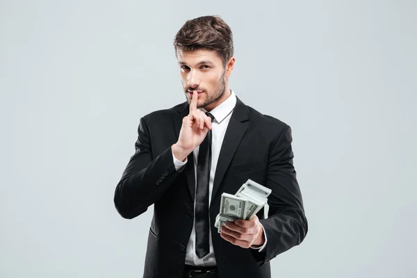 Bonito jovem empresário segurando dinheiro e mostrando sinal de silêncio — Fotografia de Stock