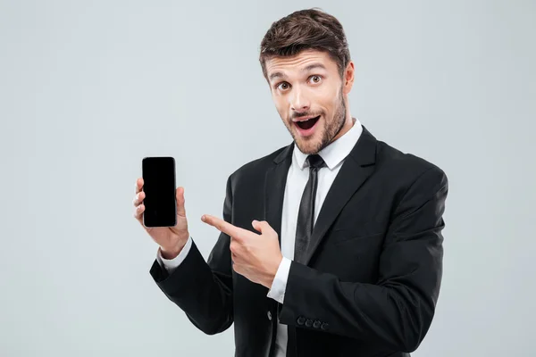 Joven empresario sorprendido sosteniendo y señalando en el teléfono inteligente de pantalla en blanco — Foto de Stock