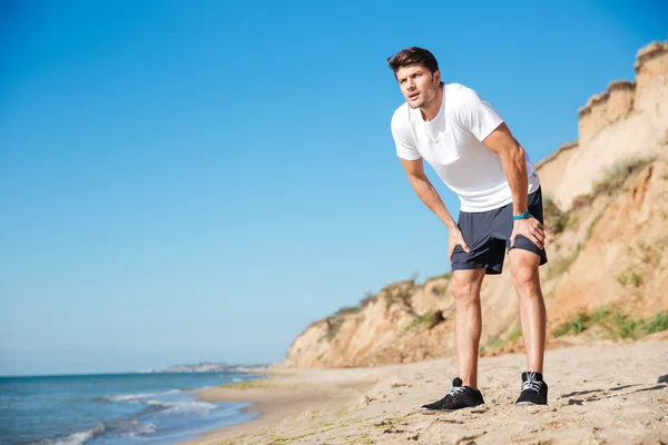 Pohledný sportovec, stojící na pláži — Stock fotografie