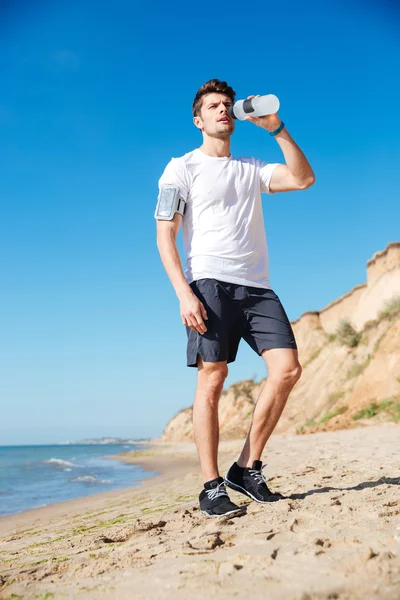 Desportista de pé e água potável na praia — Fotografia de Stock