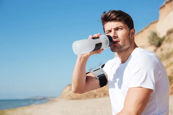 Sportler sitzt und trinkt Wasser am Strand — Stockfoto