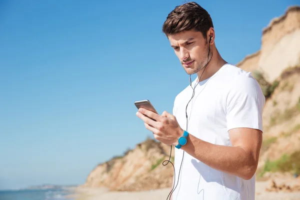 Αθλητικός τύπος χρησιμοποιώντας smartphone και να ακούτε μουσική στην παραλία — Φωτογραφία Αρχείου