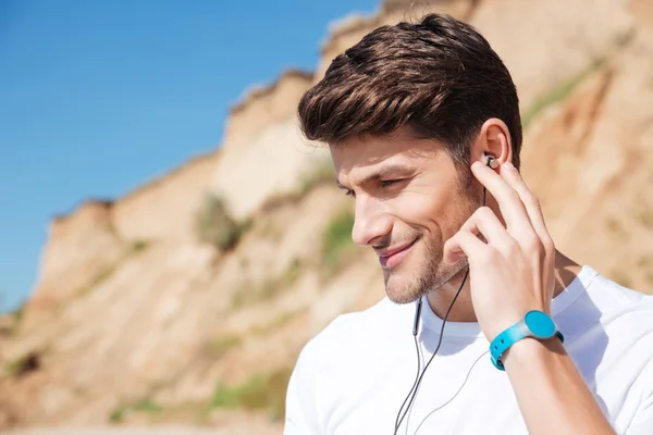 Glimlachende man in koptelefoon luisteren naar muziek op het strand — Stockfoto