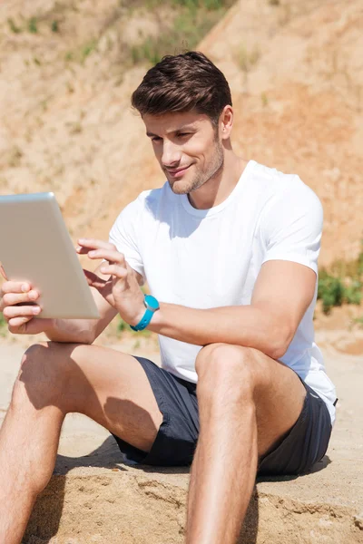 Usmívající se mladý muž pomocí tabletu na pláži — Stock fotografie