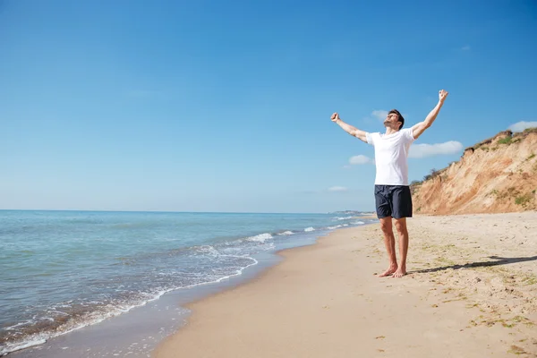 Homem feliz de pé descalço na praia com as mãos estendidas — Fotografia de Stock