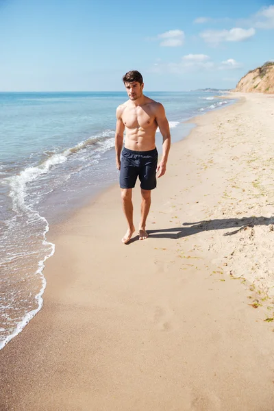 Pohledný sportovní mladý muž, procházky po pláži — Stock fotografie