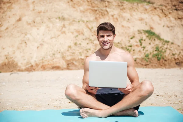 陽気な若い男がビーチでノート パソコンを使用して — ストック写真