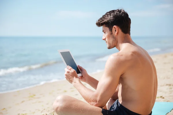 Bello uomo che utilizza tablet schermo bianco sulla spiaggia — Foto Stock