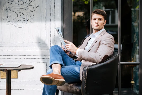 Pensive young man reading magazine in outdoor cafe