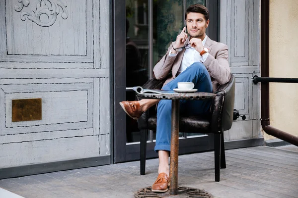 Oturma ve cep telefonu üzerinde açık kafede konuşurken adam — Stok fotoğraf