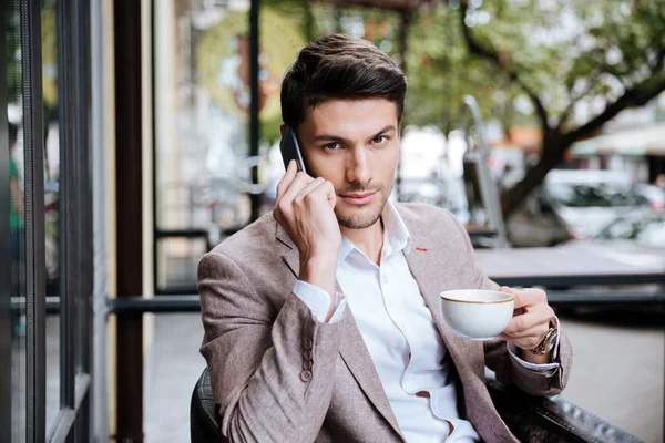 Businessman talking on cell phone and drinking coffee in cafe — Stock Photo, Image