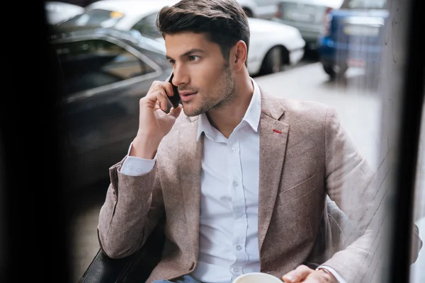 Бізнесмен розмовляє по мобільному телефону, сидячи на відкритому повітрі в кафе — стокове фото