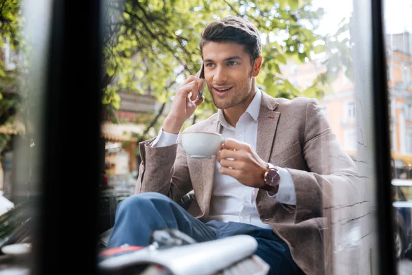 Чоловік розмовляє по мобільному телефону і п'є каву в кафе — стокове фото