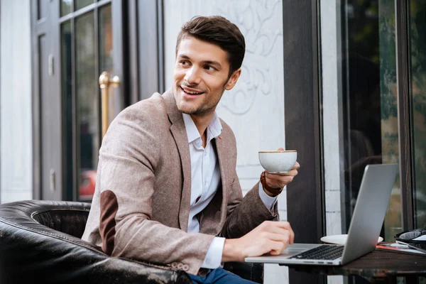 Empresario sosteniendo la taza de café y trabajando con el ordenador portátil al aire libre — Foto de Stock