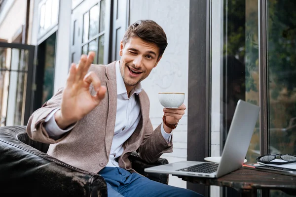 Hombre mostrando signo de ok y el uso de ordenador portátil en la cafetería al aire libre — Foto de Stock