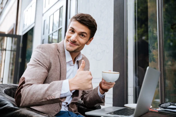 Empresario sosteniendo la taza de café y trabajando con el ordenador portátil al aire libre — Foto de Stock