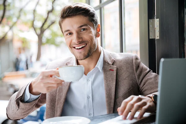 Empresario sosteniendo taza de café y trabajando con el ordenador portátil en el interior — Foto de Stock