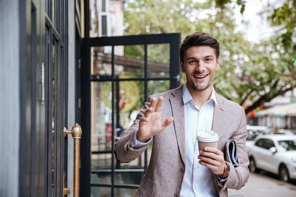 Businessman drinking cup of coffee and waving to someone — Stock Photo, Image