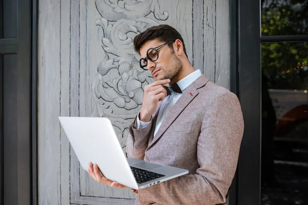 Hombre en gafas redondas divertidas pensando y usando el ordenador portátil — Foto de Stock