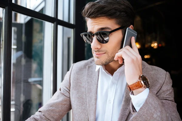 Businessman in sunglasses talking on mobile phone in cafe — Stock Photo, Image