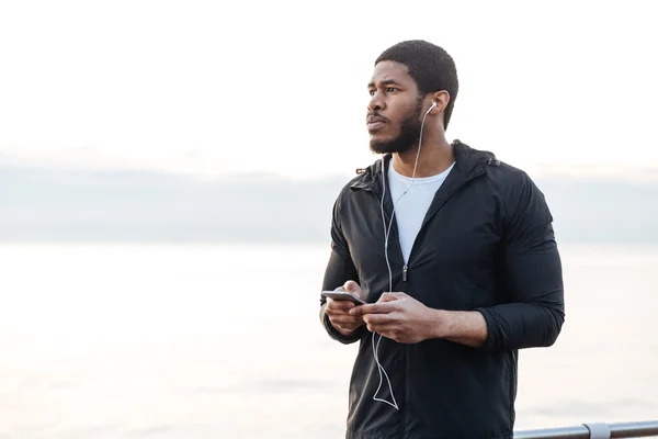 Sportsman standing and listening to music from smartphone outdoors — Stock Photo, Image