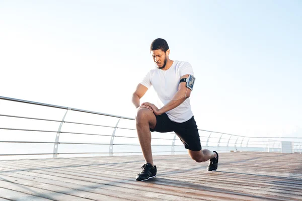 Sportsman warming up and stretching legs on pier