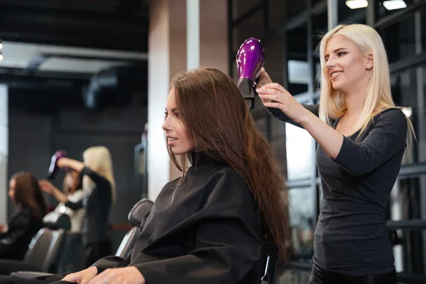 Stylist torkning håret av en kvinnlig kund på skönhetssalong — Stockfoto