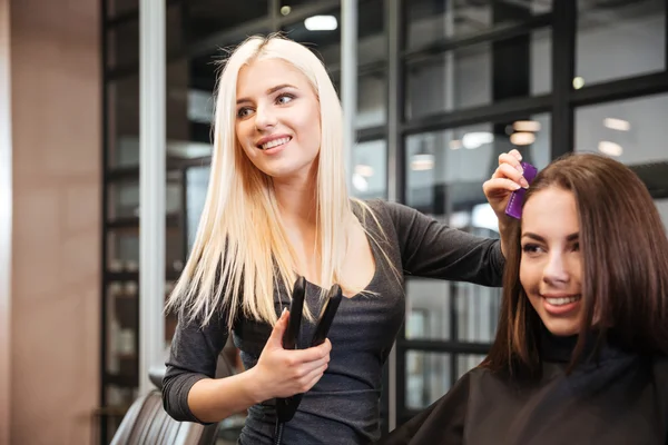 Styliste avec fer à lisser coiffant cheveux femme au salon — Photo