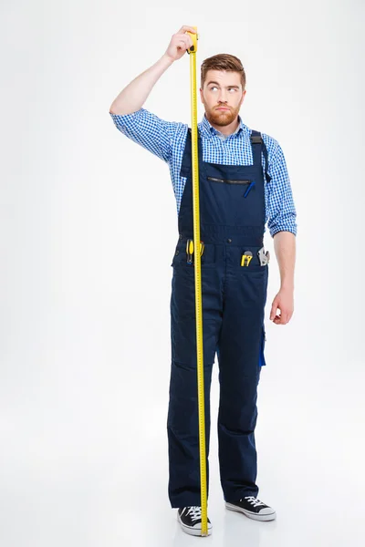 Серйозний молодий працівник стоїть і вимірює його зростання стрічкою — стокове фото