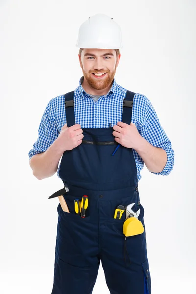 Fröhlich gutaussehender junger Bauarbeiter mit Helm steht und lächelt — Stockfoto