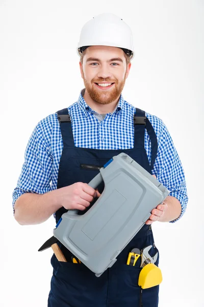 Sonriente joven trabajador barbudo en caja de herramientas de retención de casco —  Fotos de Stock