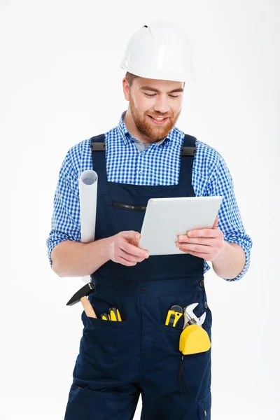 Glücklich gutaussehender junger Bauarbeiter im Helm stehend und mit Tablet — Stockfoto