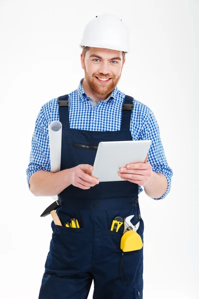 Vrolijke aantrekkelijke bebaarde man in helm lachend en met behulp van Tablet PC — Stockfoto