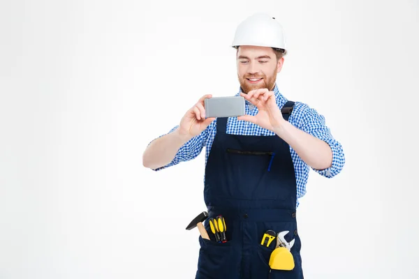 Feliz atraente jovem construtor no capacete tirar fotos usando smartphone — Fotografia de Stock