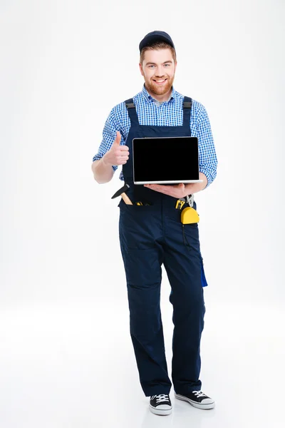 Homem construtor segurando laptop tela em branco e mostrando polegares para cima — Fotografia de Stock