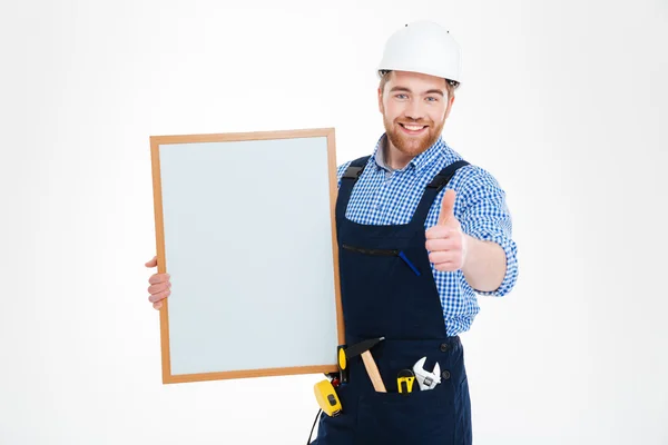 Alegre jovem construtor segurando quadro branco em branco e mostrando polegares para cima — Fotografia de Stock