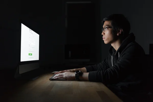 Beau asiatique jeune l'homme à l'aide de l'ordinateur dans sombre chambre — Photo