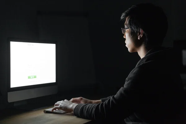 Fokussierter asiatischer junger Mann arbeitet mit Computer im dunklen Raum — Stockfoto