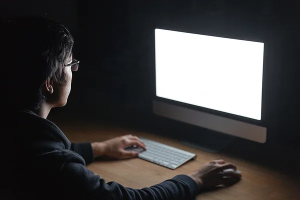 Hombre sentado en la mesa y el uso de la computadora en la habitación oscura —  Fotos de Stock