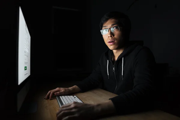 Verbaasd Aziatische jongeman werken met computer in donkere kantoor — Stockfoto