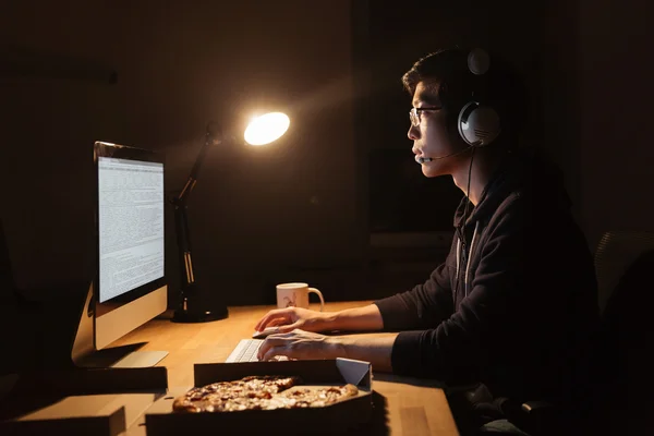 Man arbetar med dator och äta pizza i mörka kontor — Stockfoto