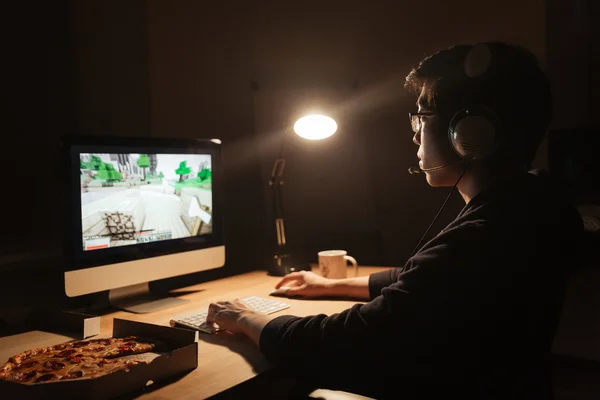 Αρσενικό gamer παίζει παιχνίδι στον υπολογιστή και να τρώει πίτσα — Φωτογραφία Αρχείου